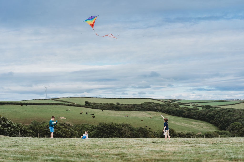 Children flying kites in the meadow with Cornish hills beyond